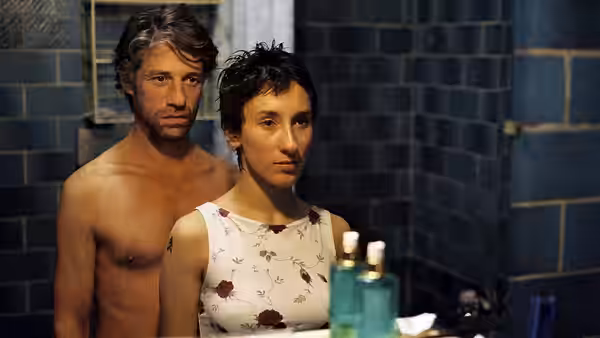 Cahit Tomruk (Birol Ünel) stands shirtless behind Sibel Güner (Sibel Kekilli) in a tiled bathroom
