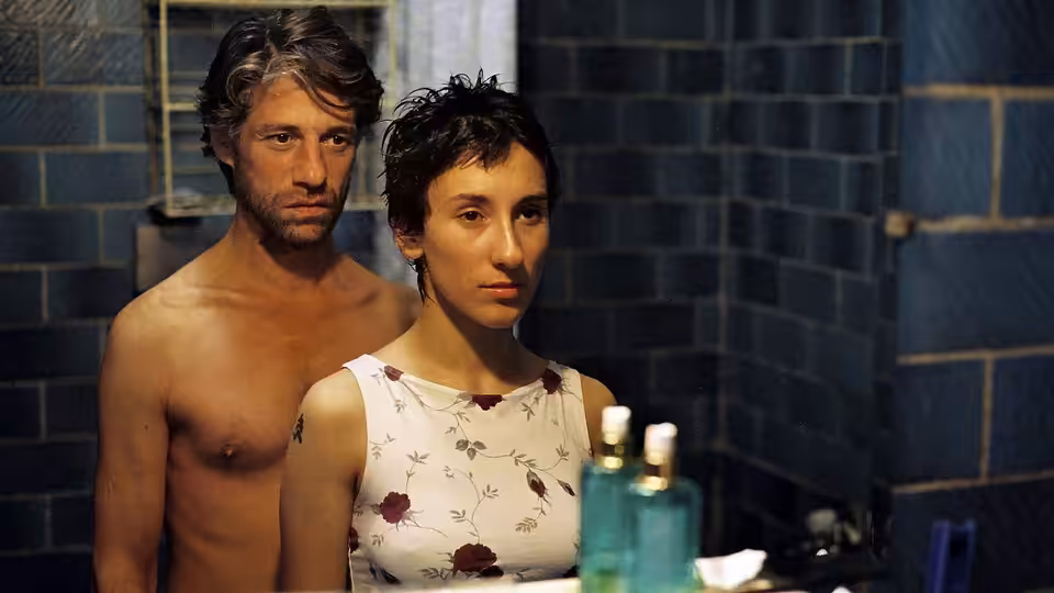 Cahit Tomruk (Birol Ünel) stands shirtless behind Sibel Güner (Sibel Kekilli) in a tiled bathroom
