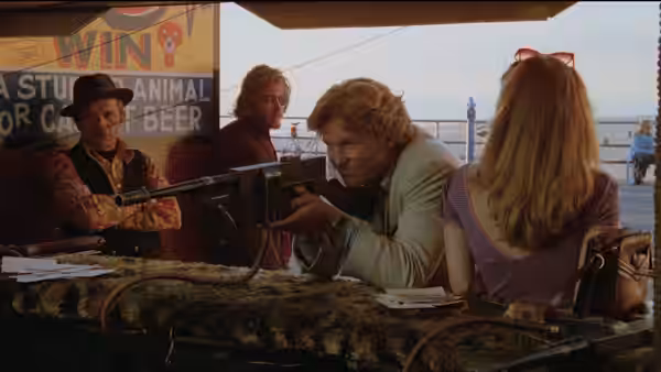 Alex Cutter (John Heard) aiming a rifle on a pier with others nearby