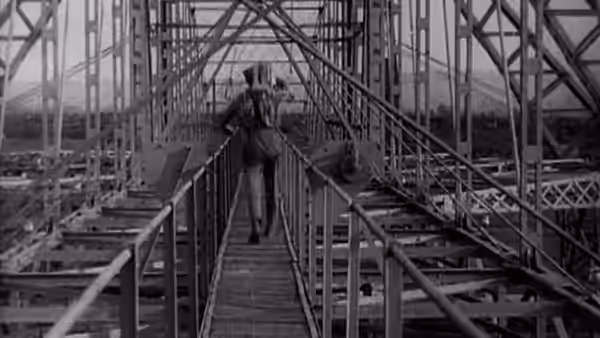 A man walks away along a raised metal walkway between industrial structures