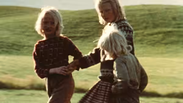 Three children holding hands while walking across a grassy hillside