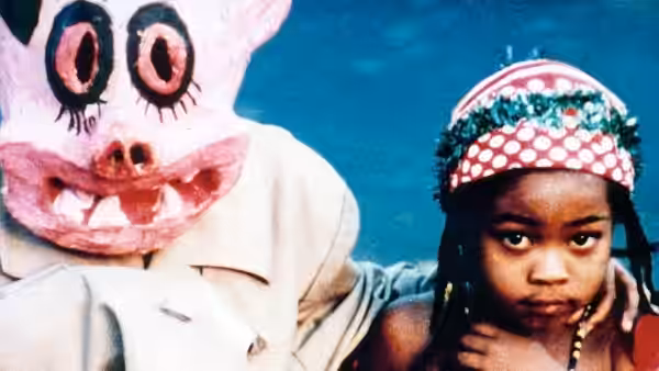 Young girl beside an adult wearing a large pink pig mask
