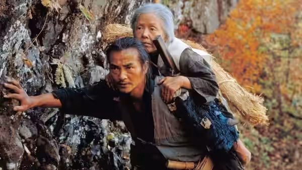 Tatsuhei (Ken Ogata) carrying Orin (Sumiko Sakamoto) on his back up a rocky slope