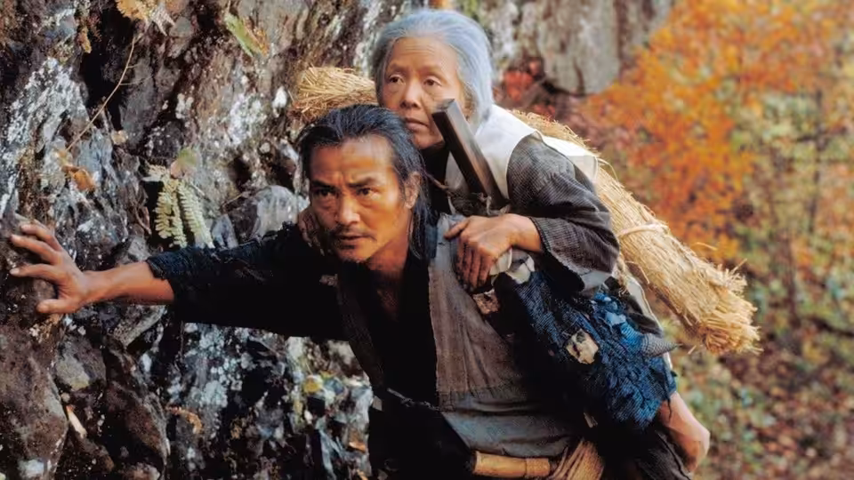 Tatsuhei (Ken Ogata) carrying Orin (Sumiko Sakamoto) on his back up a rocky slope