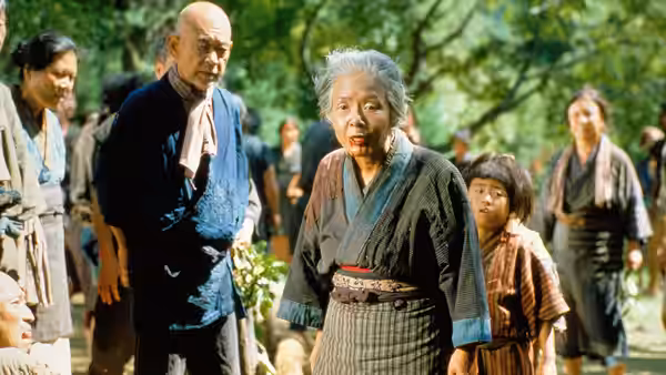 Orin (Sumiko Sakamoto) standing among villagers in a sunlit forest clearing