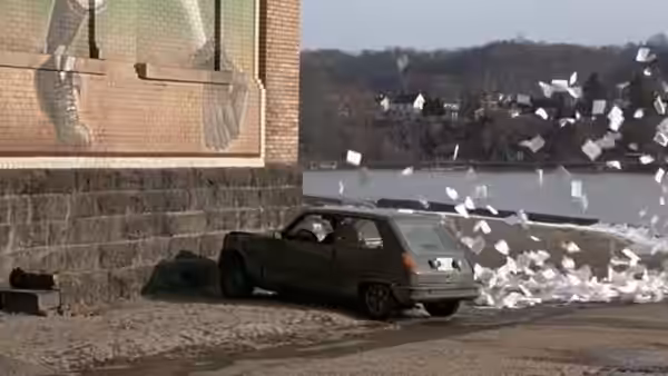 a green car parked by the water with papers blowing around