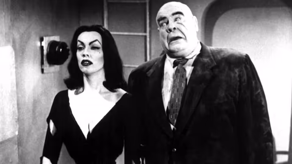 A woman in a black dress stands beside a bald man in a suit