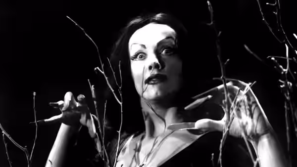 A woman with long nails raises her hands among bare branches