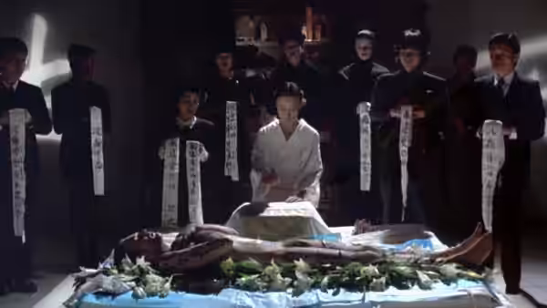 A man in white kneels beside a body as suited men hold strips of calligraphy