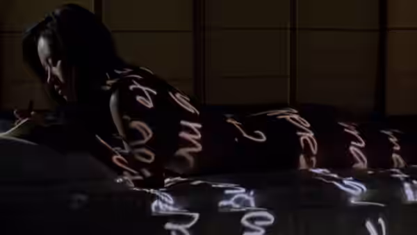 A woman lies on her stomach with calligraphy painted across her back