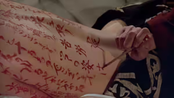 A hand writes calligraphy across a reclining woman's bare torso