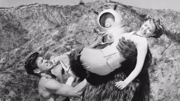 Man grapples with Ro-Man carrying a woman in rocky terrain