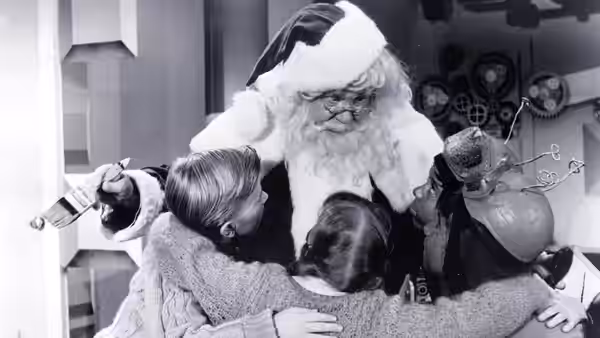 Santa Claus looks down at several children gathered around a large device