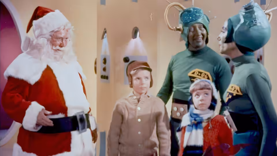 Santa Claus stands with two children facing two Martians in a corridor