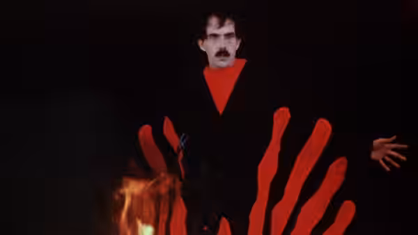 The Master stands with arms outstretched before red flames