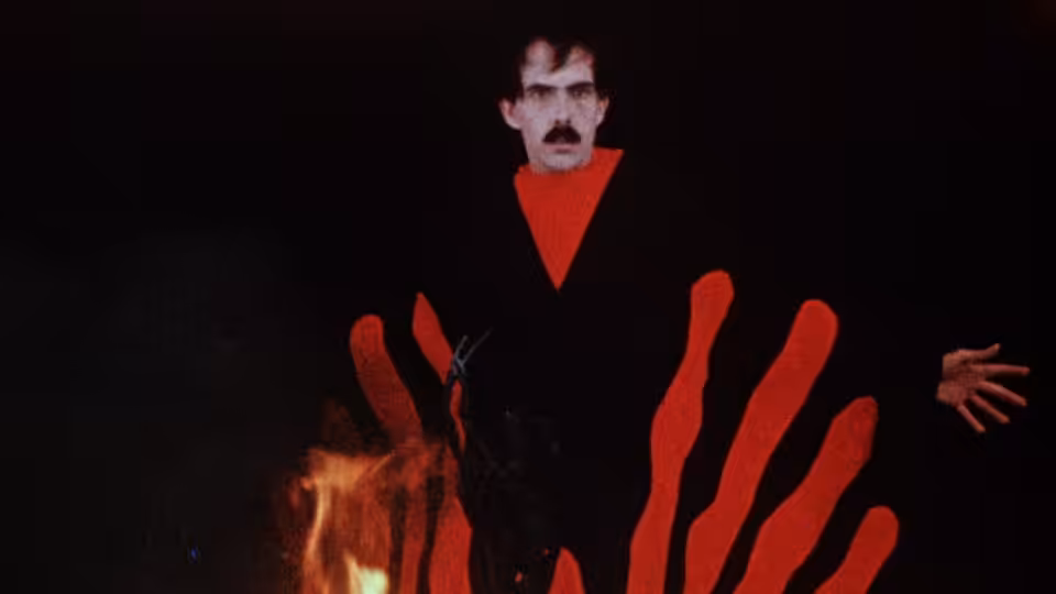 The Master stands with arms outstretched before red flames