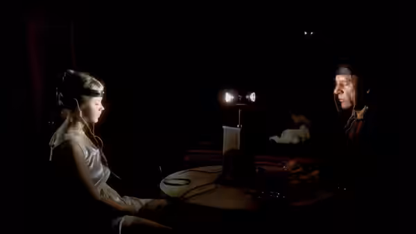 Regan (Linda Blair) with wired headband sits opposite Father Lamont (Richard Burton) at a table