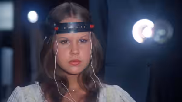 Regan (Linda Blair) wearing an electrode headband stares ahead with wires attached