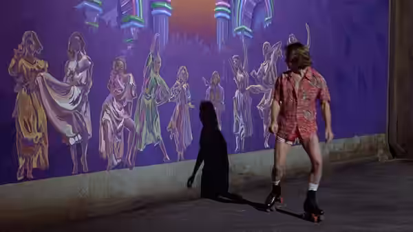 Sonny Malone (Michael Beck) on roller skates before a vibrant mural on a purple wall