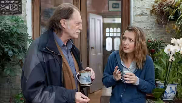 Ronnie and Mary holding mugs and talking outside a house