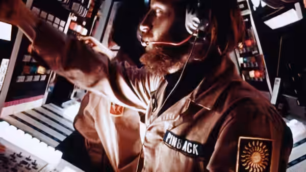 Sgt. Pinback (Dan O'Bannon) reaches across illuminated control panels in the spacecraft cockpit