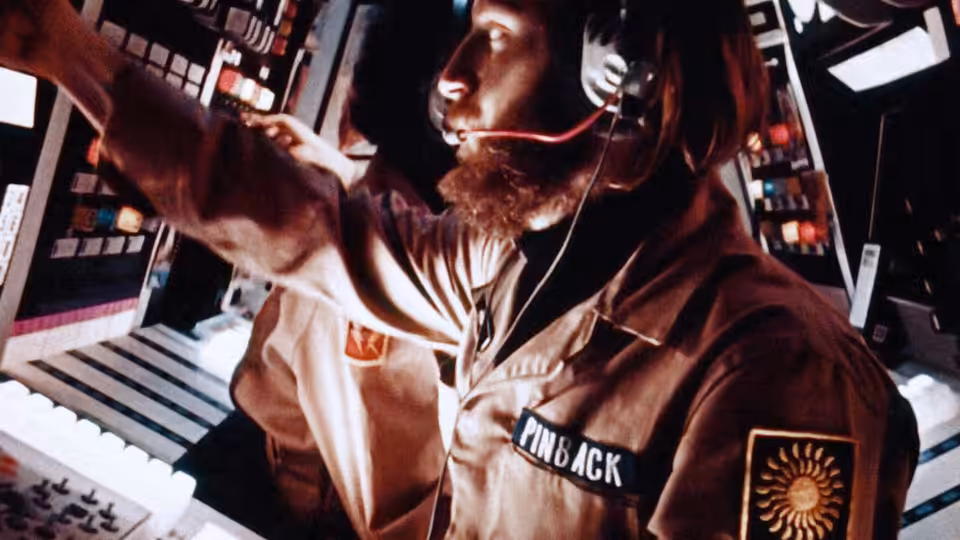 Sgt. Pinback (Dan O'Bannon) reaches across illuminated control panels in the spacecraft cockpit