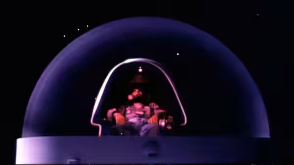 A spacesuited astronaut sits inside a rounded cockpit canopy against the darkness of space