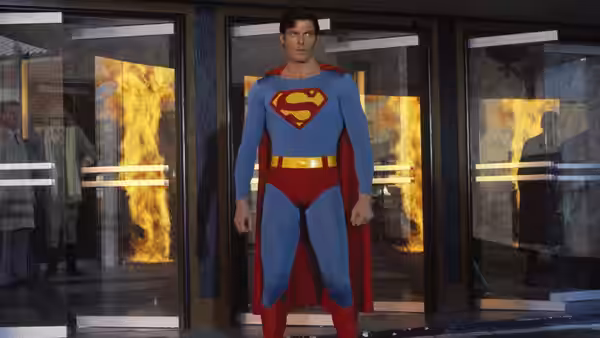 Superman (Christopher Reeve) stands before glass doors with fire visible behind