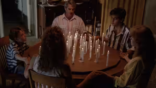 Family sits around a wooden table covered with many lit candles