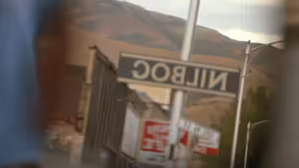 Sign reading NILBOG mounted on a pole beside buildings and hills