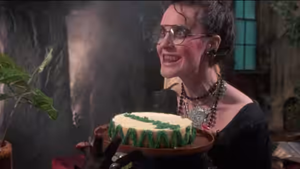 Woman with glasses smiles while holding a green frosted cake