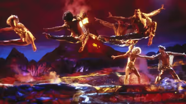 performers in gold costumes leap above a volcanic landscape at night