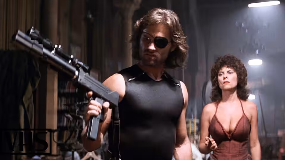Snake Plissken (Kurt Russell) holds a rifle as Maggie (Adrienne Barbeau) stands beside him
