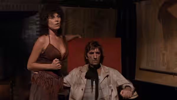 Maggie (Adrienne Barbeau) stands beside Brain (Harry Dean Stanton) in a red chair