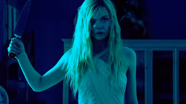 Jesse (Elle Fanning) holds a knife in a blue-lit room
