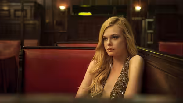 Jesse (Elle Fanning) sits alone in a red booth