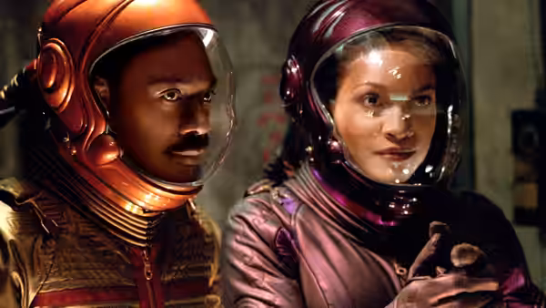 Man and woman in helmets stare ahead with serious expressions