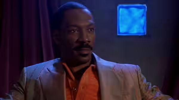 Eddie Murphy wears a shiny jacket in a dimly lit room