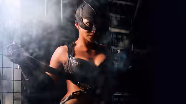 Catwoman (Halle Berry) holding a whip in a smoky industrial space