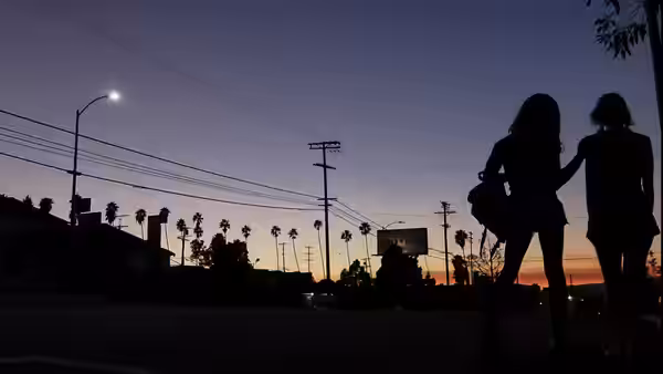 Two figures walk hand in hand along a street at sunset