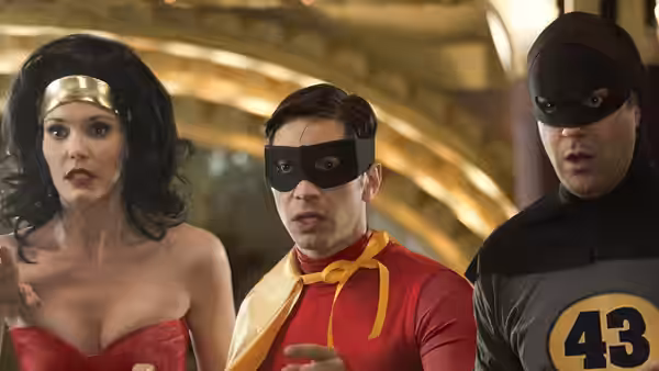 Woman in red costume with gold headband stands with two masked men indoors