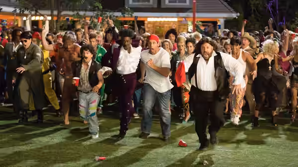 A large group of friends dances energetically on grass at an outdoor night party