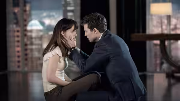 Christian Grey (Jamie Dornan) touching Anastasia Steele (Dakota Johnson) face while seated indoors