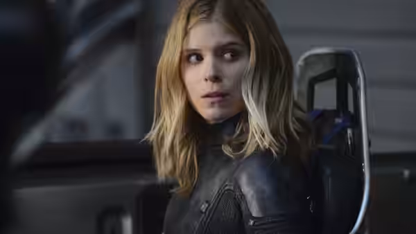 Sue Storm (Kate Mara) with blonde hair in a dark suit looking sideways