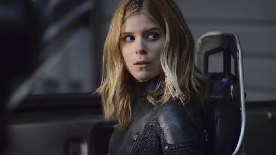 Sue Storm (Kate Mara) with blonde hair in a dark suit looking sideways