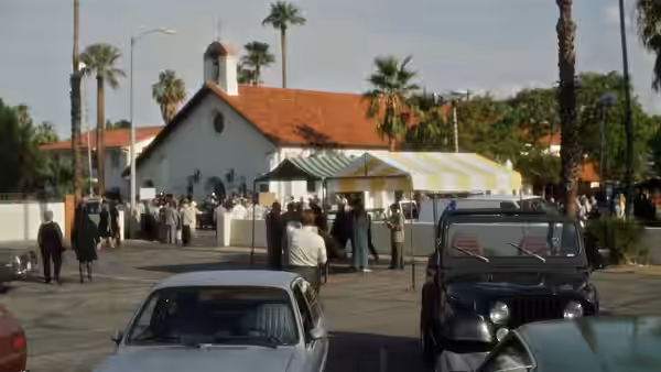 a crowd gathered outside a church with cars parked nearby