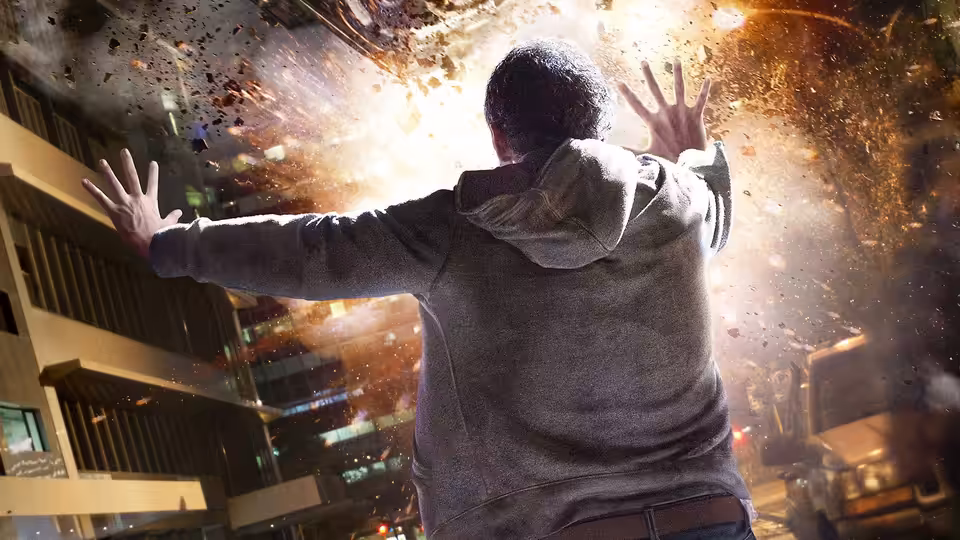Andrew Detmer raises his hands as debris bursts through the air above a city street