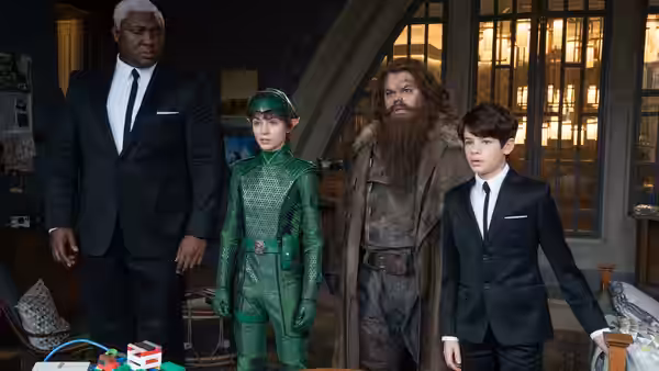 Butler (Nonso Anozie) and Artemis Fowl (Ferdia Shaw) standing with two companions indoors