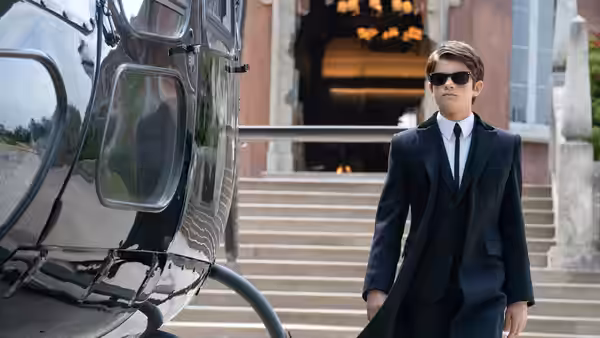 Artemis Fowl (Ferdia Shaw) beside a helicopter on steps outside a building