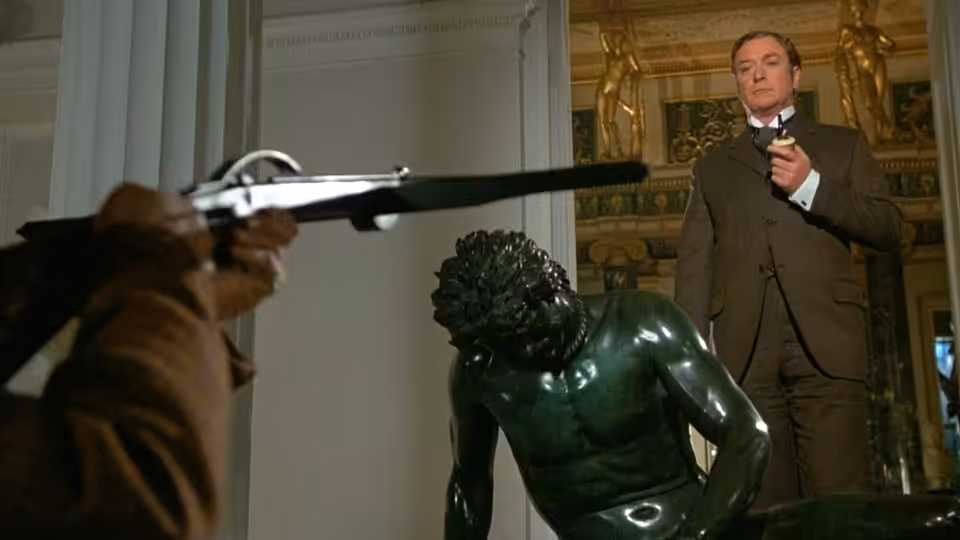 Sherlock Holmes (Michael Caine) holds a pipe as an armed man aims at him beside a statue